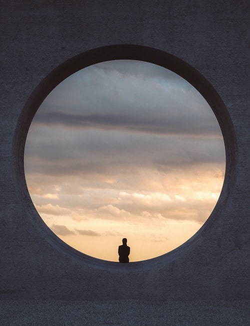 a woman sitting inside an anstract circle looking out at the clouds in the sky